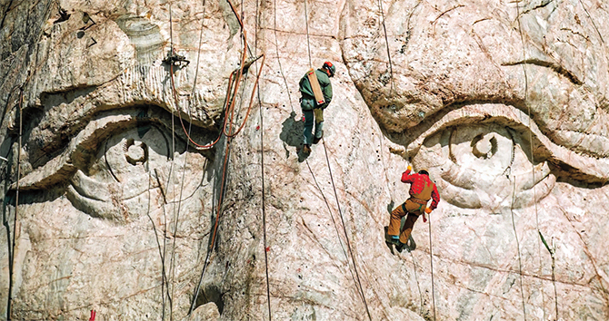 Enlargeable image of people climbing on a pair of large eyes carved into a mountain