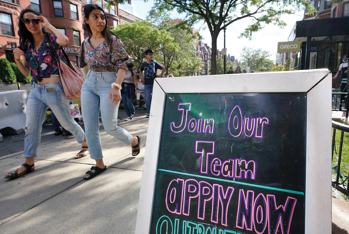 Photo of two teens walking by a sign that reads, "Join Our Team: apply now"