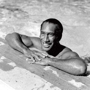 Black & white photo of Kahanamoku hanging out by the side of a pool