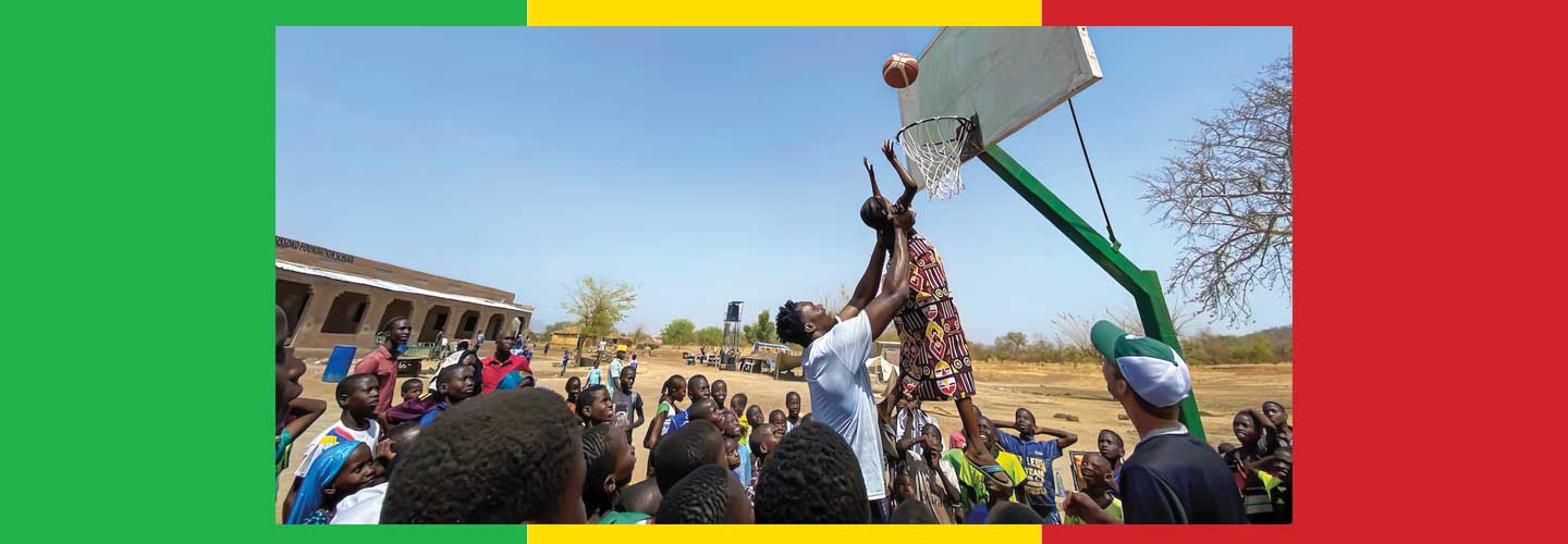 Photo of an adult helping little kids score a hoop in basketball