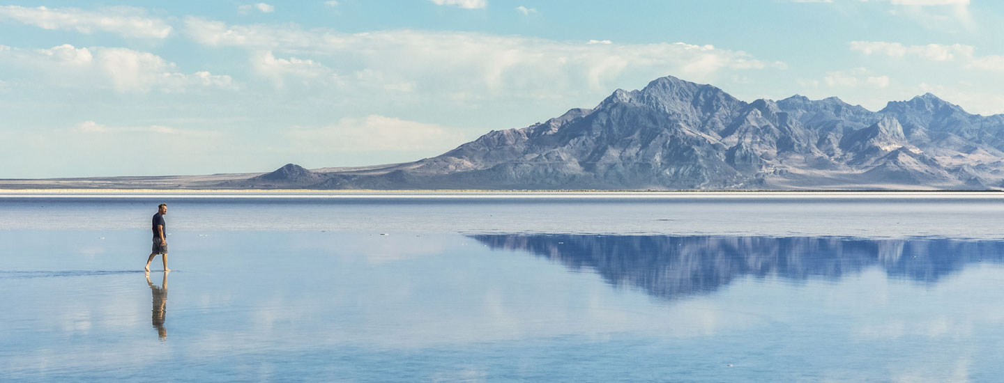 Photo of a person walking on a mirror-like surface against backdrop of mountain range